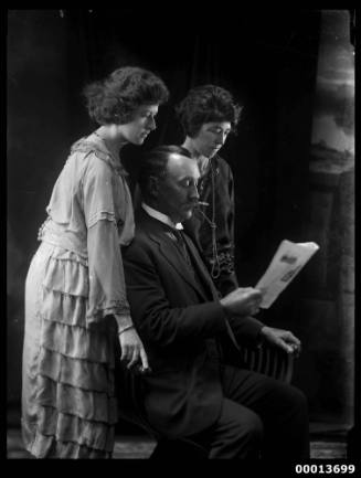 Group portrait featuring two ladies and a man reading a paper