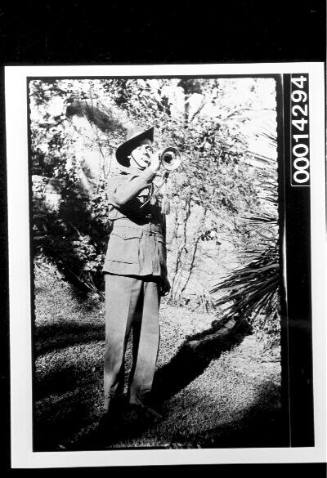An Australian soldier plays a bugle in a garden