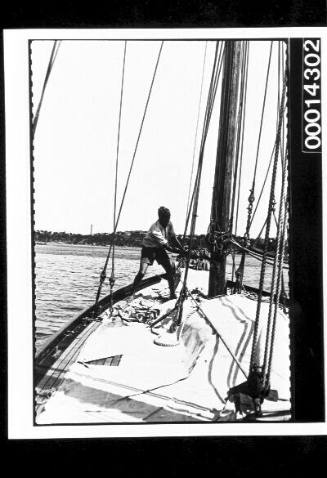 A man attends to ropes on a yacht, sails lay on the deck