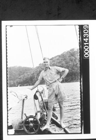 Young man standing at the cockpit of a yacht, dinghies in tow