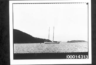 Yacht moored in calm waters, headland in the distance