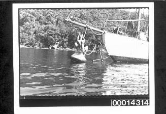 Man balancing on a mooring buoy by holding onto a yacht's bowsprit rope