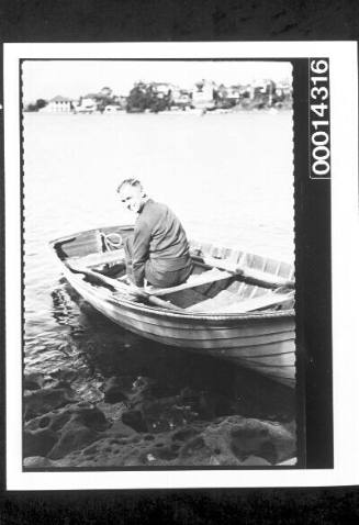 Man seated in a dinghy at the waters edge