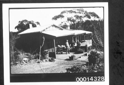 Three people standing on the verandah of a house surrounded by bush