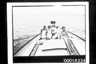 Men and women sitting at the stern of a yacht, dinghy in tow