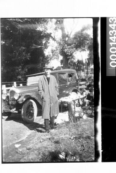 Man wearing a coat and hat stands beside a car