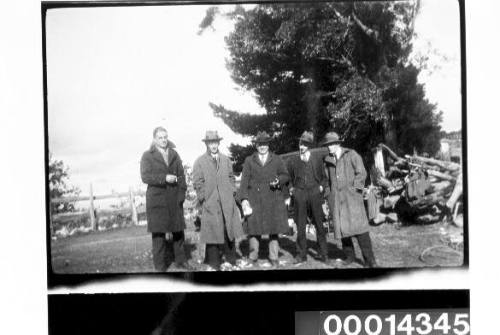 Group of men wearing coats and hats in a garden