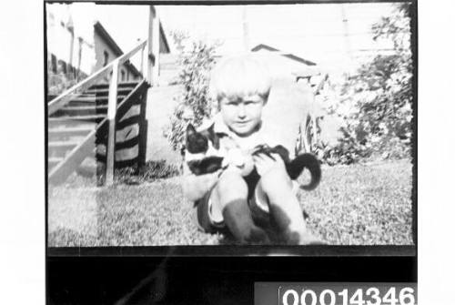 Sitting in a garden a young boy holds a cat