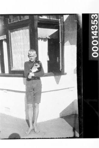 Young boy holding a cat outside a home