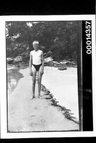 A boy in bathers standing on a sandy shore