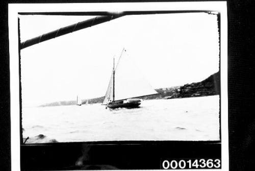 Small yacht under sail with crew on deck along a coastal strip