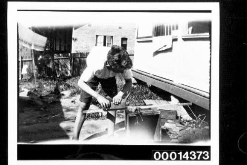 A boy planing wood in a backyard