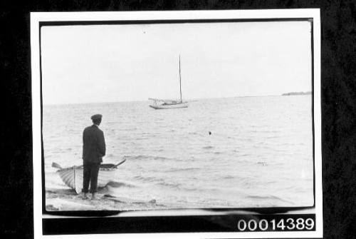 Man beside a dinghy on the beach looking out toward a yacht