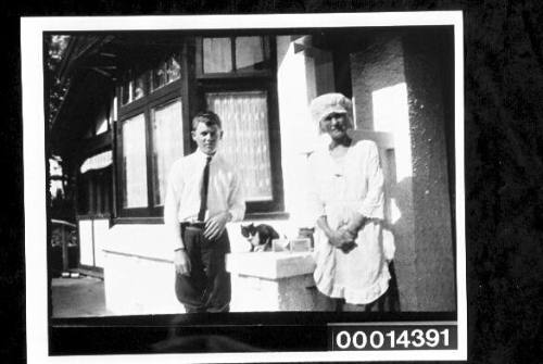 A young man poses with a cat and woman outside a home