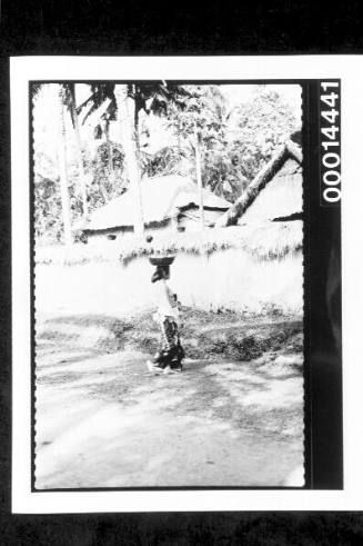 Balinese women carrying a basket on her head along a dirt road, Indonesia