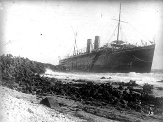 A twin funnel passenger ship aground on a rock covered beach