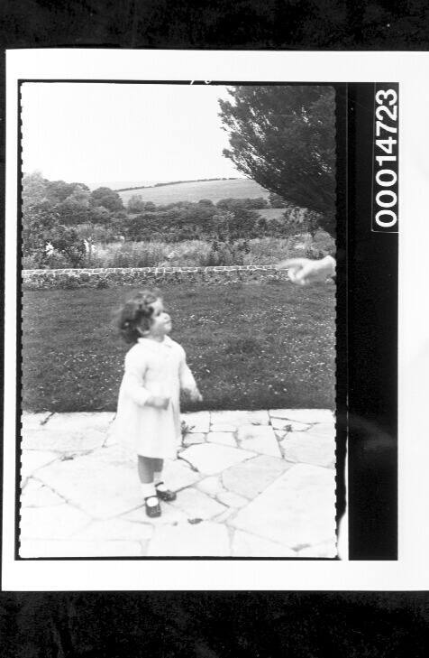 A young child on a paved garden path, the English countryside in the background