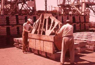 Slide depicting two men assisting a crane to collect cargo from the wharf