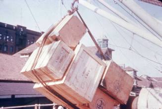 Slide depicting a stack of wooden crates being lifted by a crane