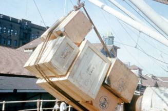 Slide depicting wooden boxes being hoisted by a crane