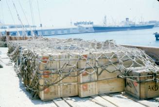 Slide depicting the deck of a ship with wooden crates and cargo netting