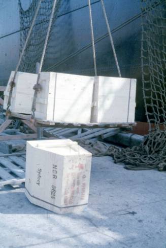 Slide depicting a stack of wooden crates lifted onto the deck of a vessel one has fallen off