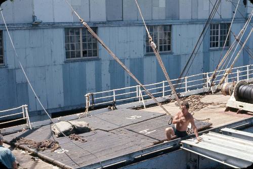 Slide depicting men working on deck with wharf building visible