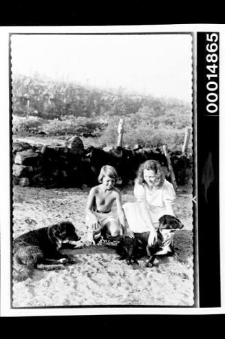 A young girl and woman kneel with their two dogs on a Galapagos Islands beach