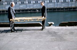 Slide depicting men dressed in suits carrying a metal yellow stretcher