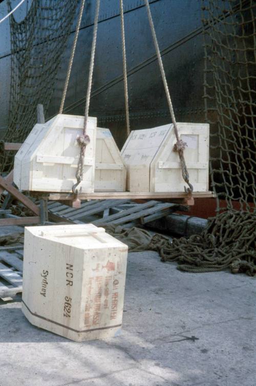 Slide depicting six wooden crates being unloaded from a ship