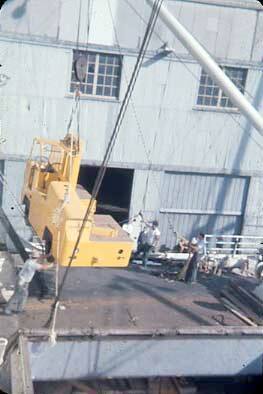Slide depicting men guiding a vehicle being lifted by crane onto ship