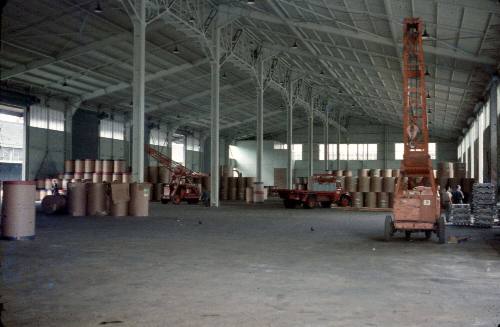 Slide depicting stacked barrels and machinery in a warehouse