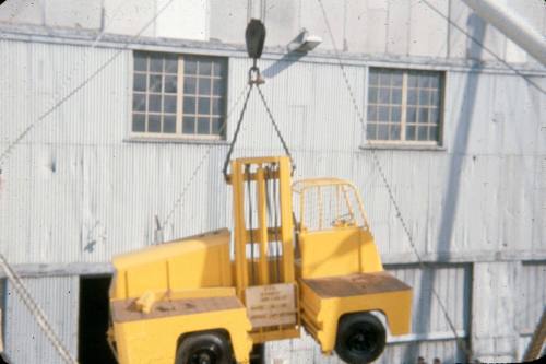 Slide depicting a yellow vehicle suspended by crane