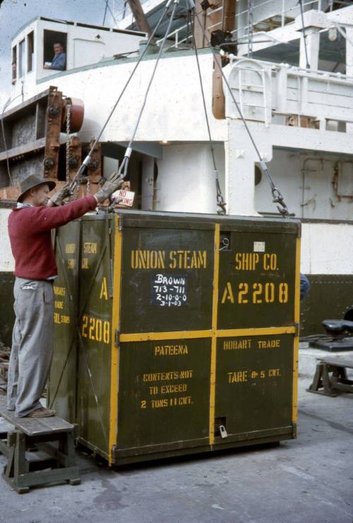 Slide depicting a man affixing cables to the corners of a metal box for transport to ship