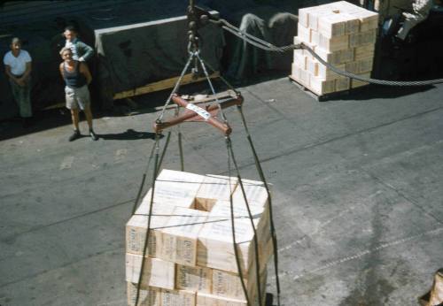 Slide depicting stacked boxes on a pallet on the ground about to be lifted by crane