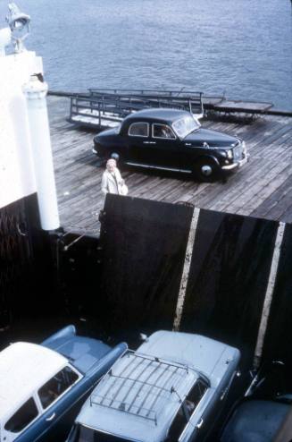 Slide depicting a cargo ship containing cars along side a wooden wharf