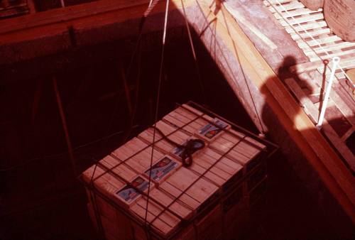 Slide depicting stacked fruit crates bound with rope being lowered into cargo hold