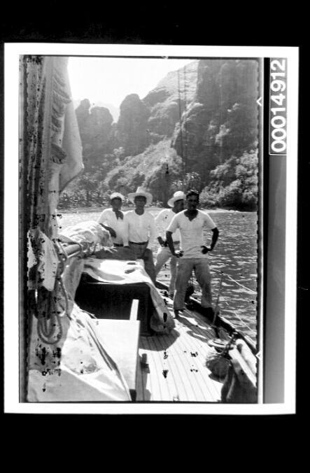 Four men stand on the deck of a yacht not far from the rocky cliffs of Fatu Hiva Island