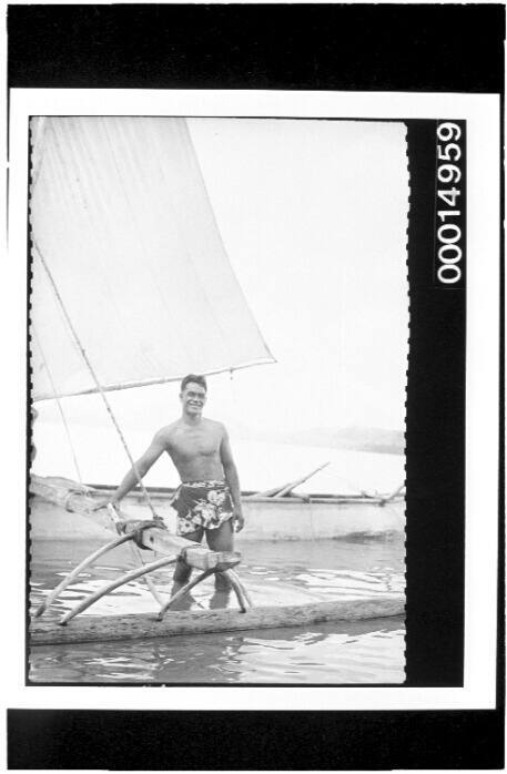 A man stands beside an outrigger sailing craft, Bora Bora