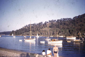 Image of three people sitting on a boat hull on a beach