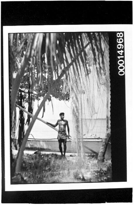 A Polynesian man standing in front of his fishing boat on a beach in Bora Bora