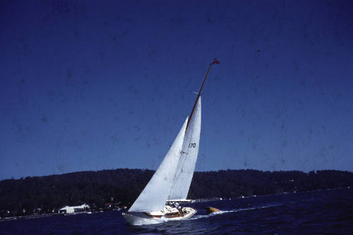 Image of a boat sailing wit reefed sails and towing a red dinghy behind