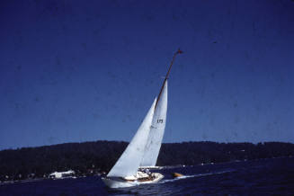 Image of a boat sailing wit reefed sails and towing a red dinghy behind