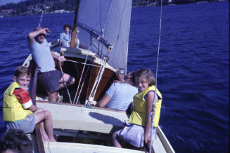 Image of two children wearing life jackets and three adults on a sail boat under sail