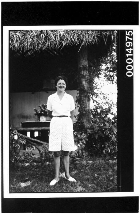 A young woman poses for the camera standing outside a thatched roof hut in Tahiti