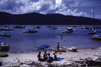 Image of people sitting on Hallett's Beach with boats in the background