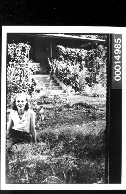 A woman sits in the garden at the front of a home in Tahiti