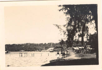 Photograph depicting men walking along the shore in front of a tropical coastal village