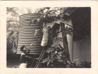 Photograph depicting two men next to a water tank outside a house