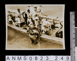 Silver gelatin photograph featuring group of sailors on board small craft with diver emerging from water